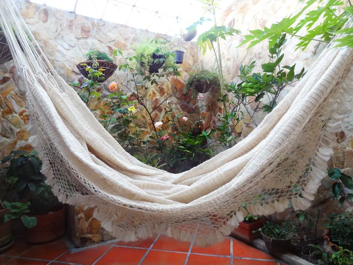 Chinchorro de curagua colgado en un patio luminoso con plantas y suelo de terracota